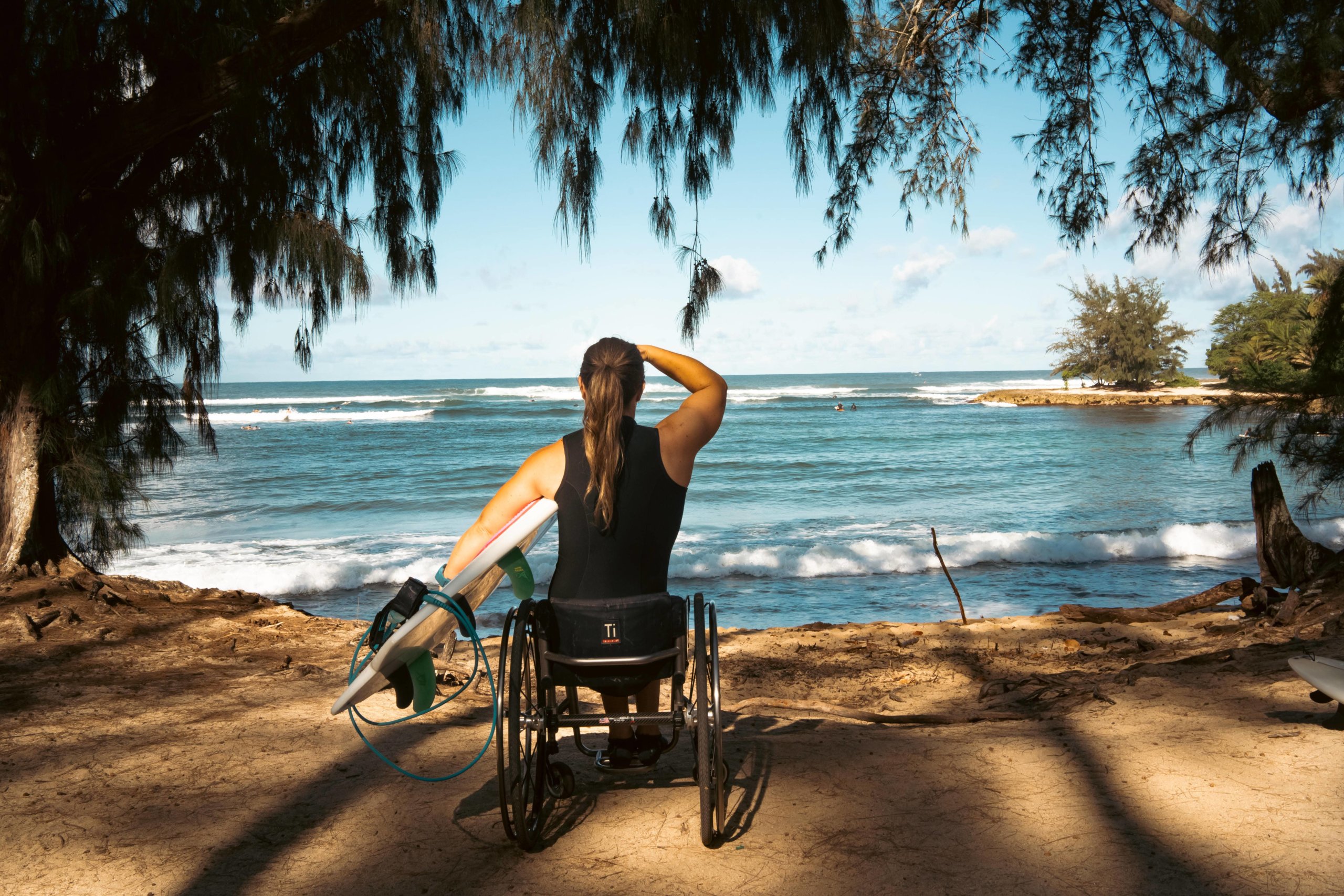 Victoria Feige on beach in her wheelchair with her surfboard