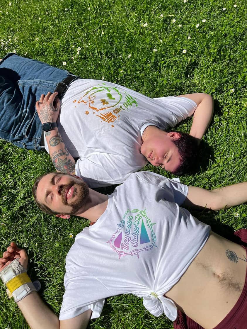 Alex Gray and friend laying in green grass wearing GNDR SHREDR shirts.