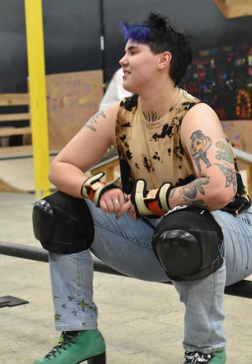 Alex Gray sitting at park with knee pads and rollerskates.